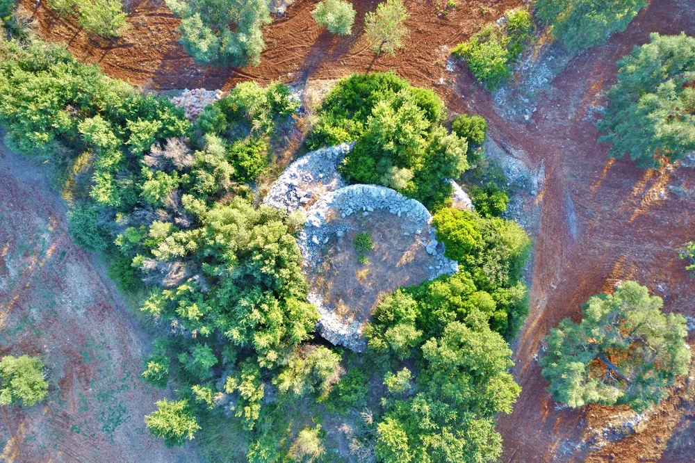 Luftaufnahme einer specchia, eines megalithischen Trockensteinhügels, zwischen Olivenhainen bei Ceglie Messapica, Apulien