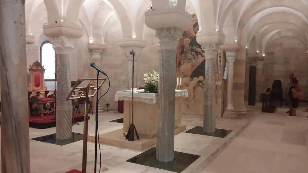 Die Krypta unter der Kathedrale von Otranto, ungleiche Marmorsäulen unter Kreuzgewölben, ein Altar mit Blumen und ein mittelalterliches Fresko an der Wand